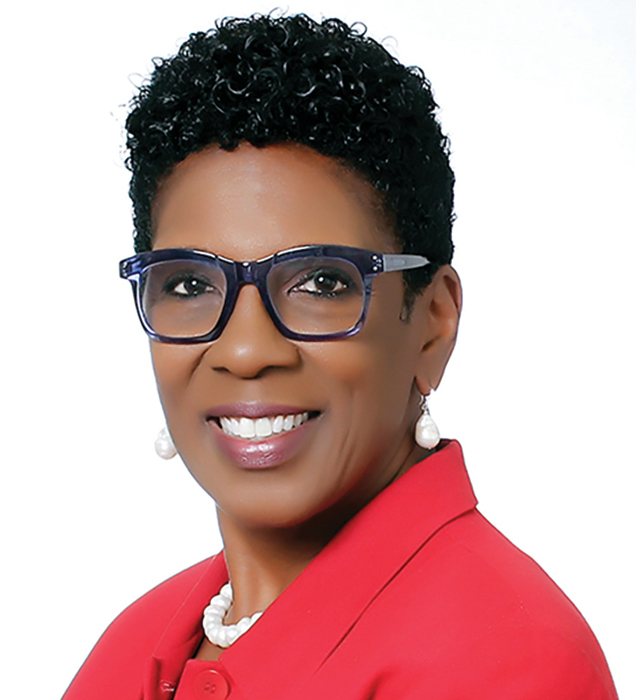 A Black woman with short hair and glasses smiling headshot wearing a red suit