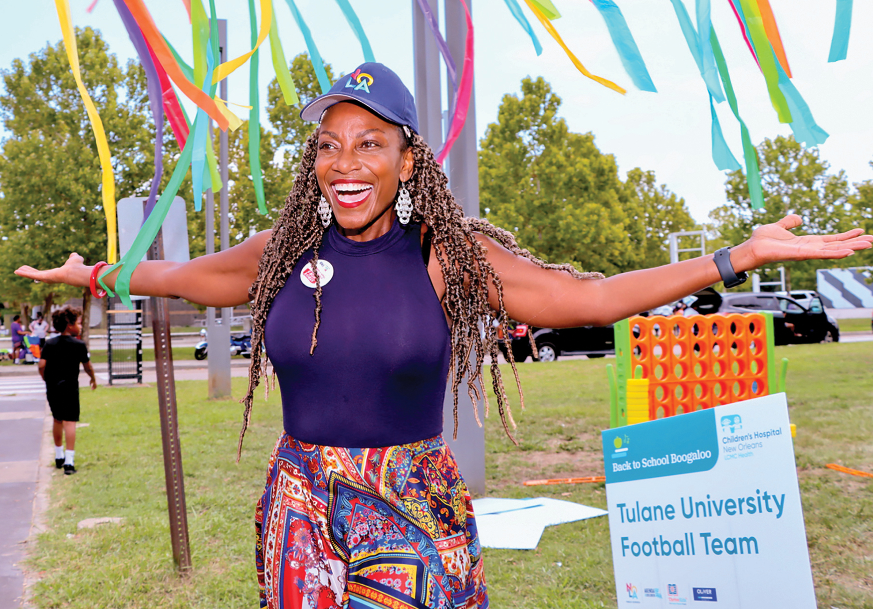 A Black woman with long hair smiling with her arms outstretched outdoors