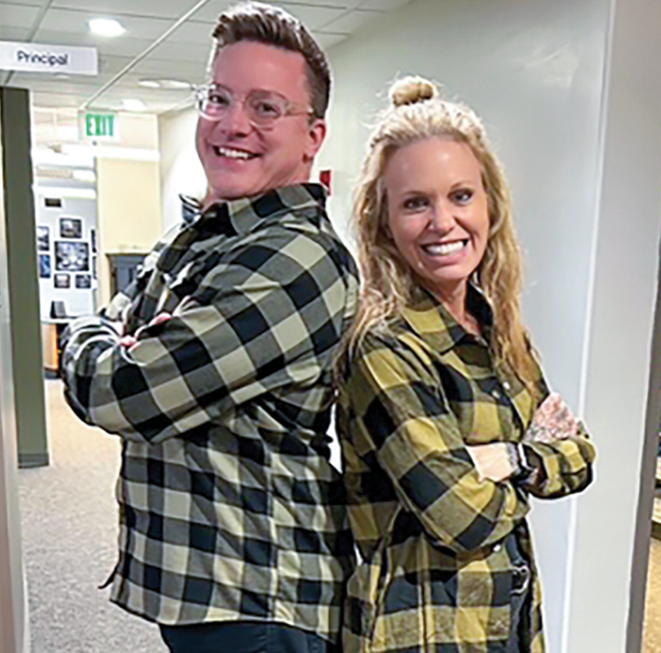 A white man and woman back to back wearing flannel shirts and smiling