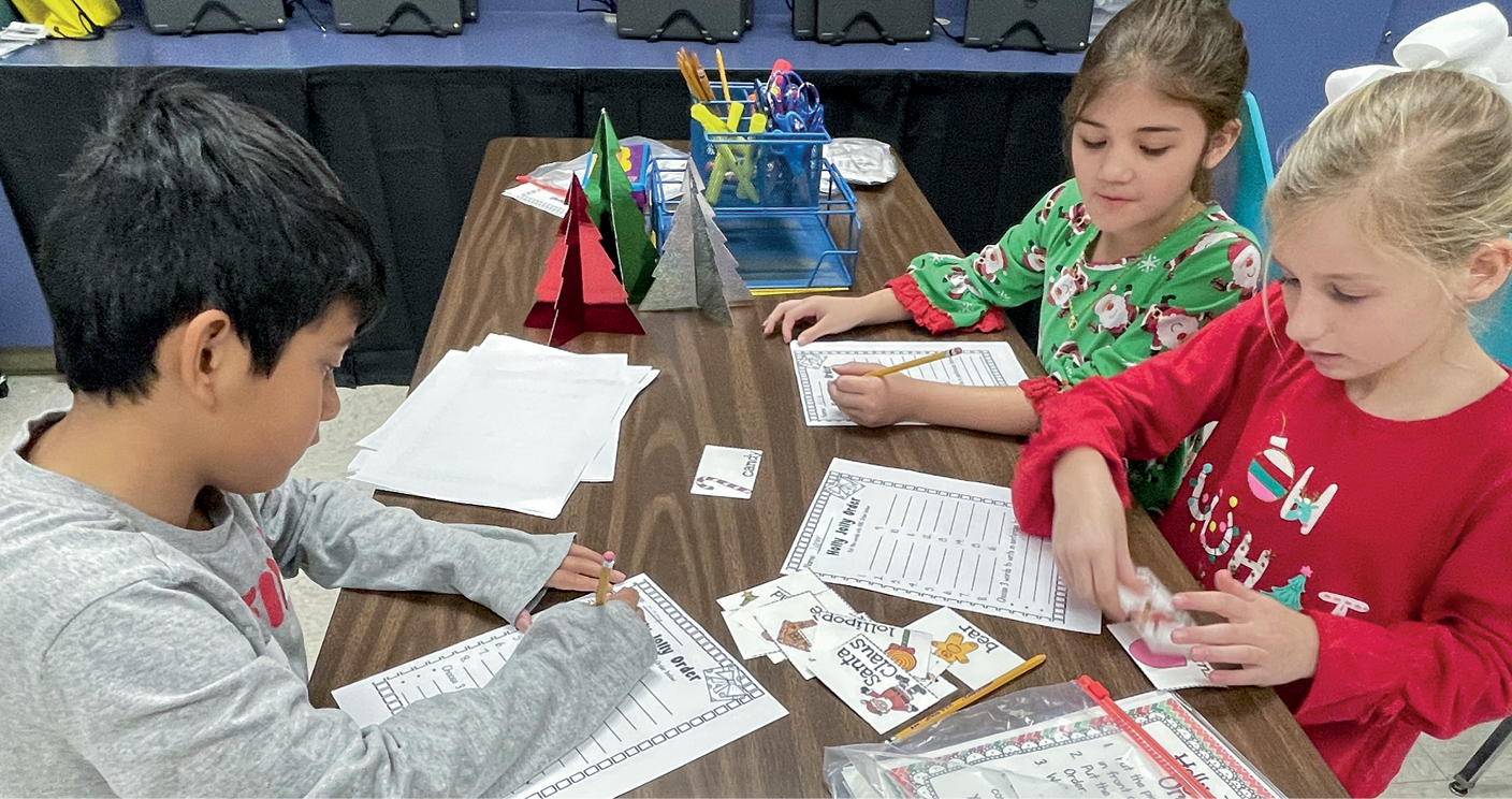 Three children at a table working on paper materials