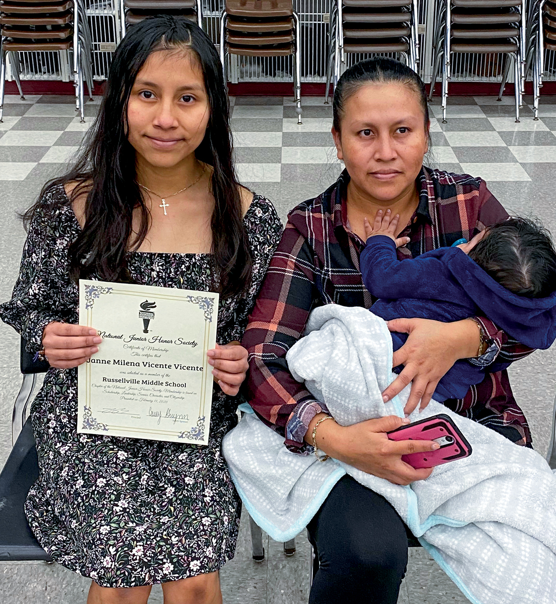 A middle school student holding up a certificate sitting next to her mother