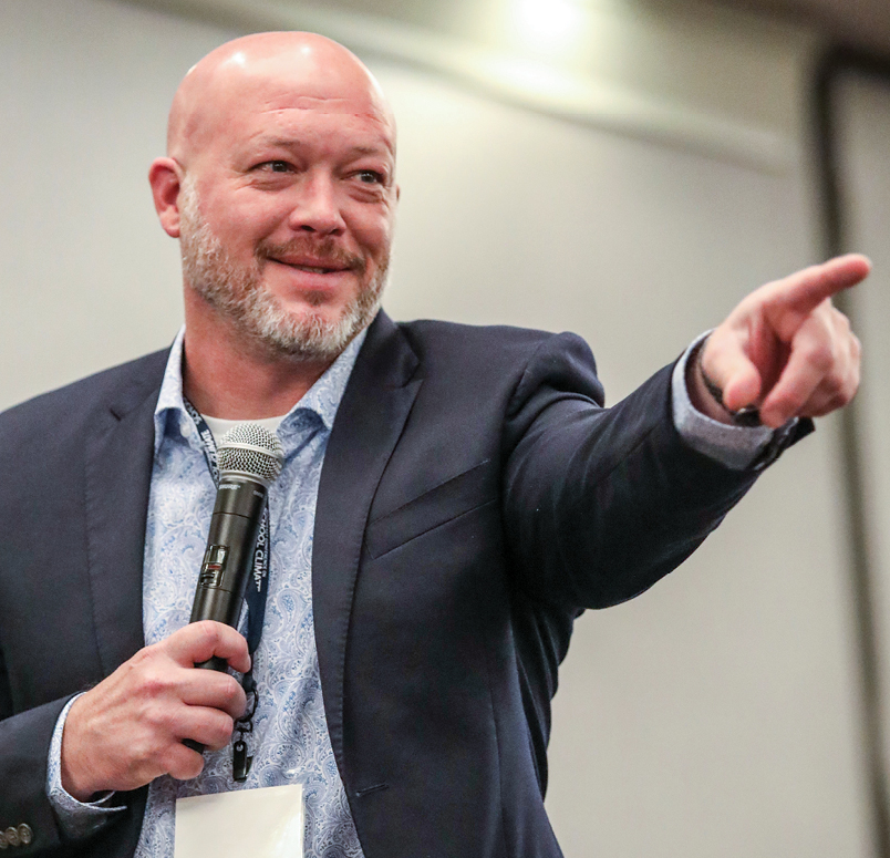 A white man holding a microphone, pointing and smiling
