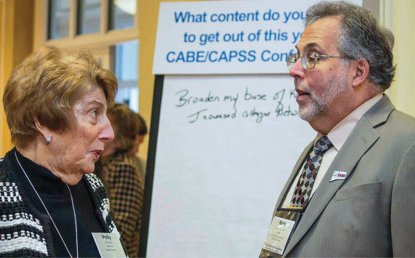 A white woman and white man talking with a big notepad board behind them