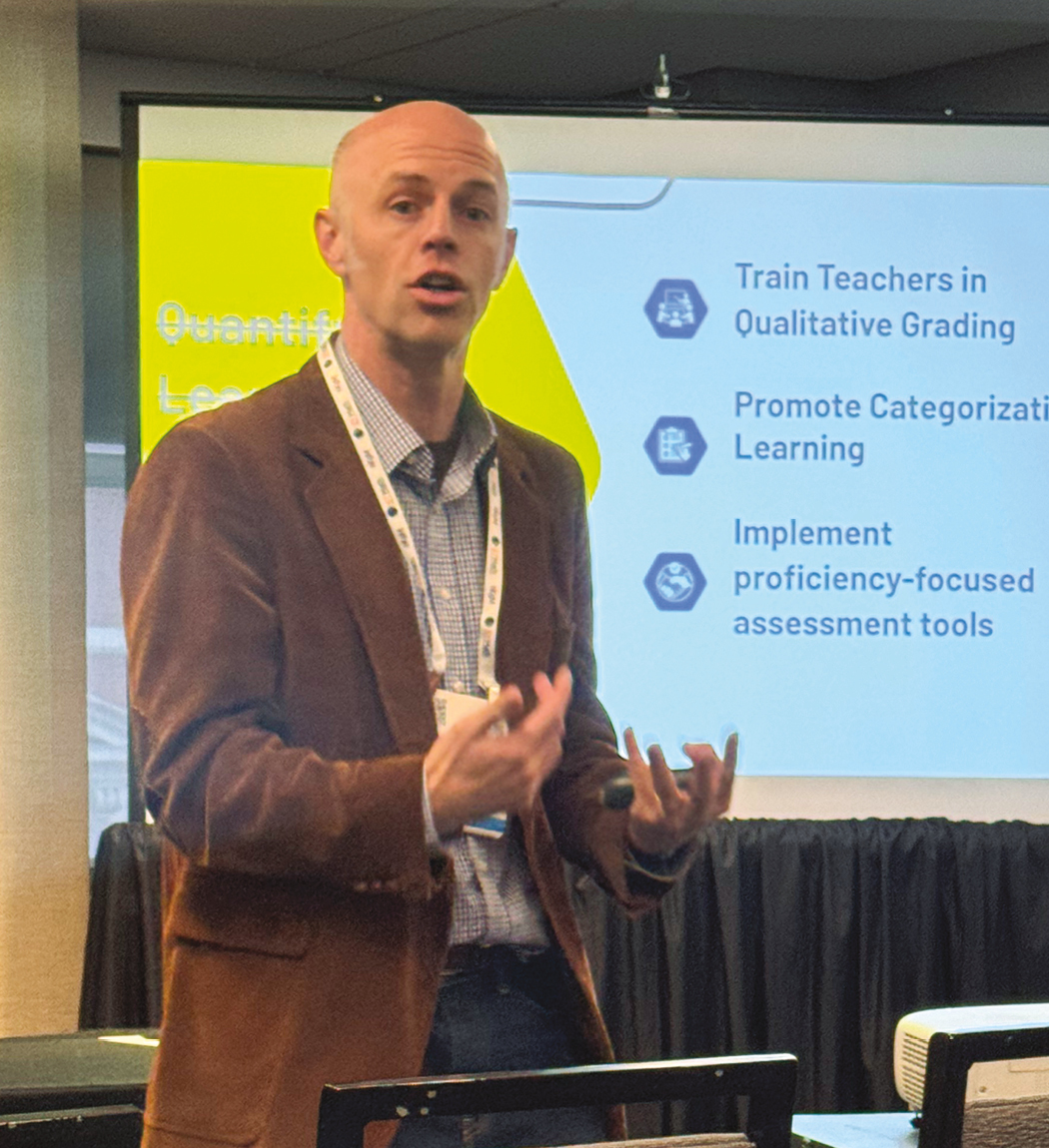 A man wearing a brown jacket presenting in front of a screen