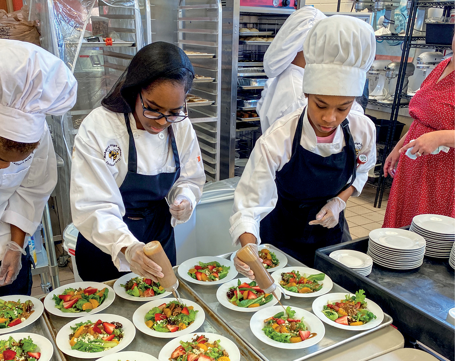 Students wearing culinary uniforms and aprons plate food