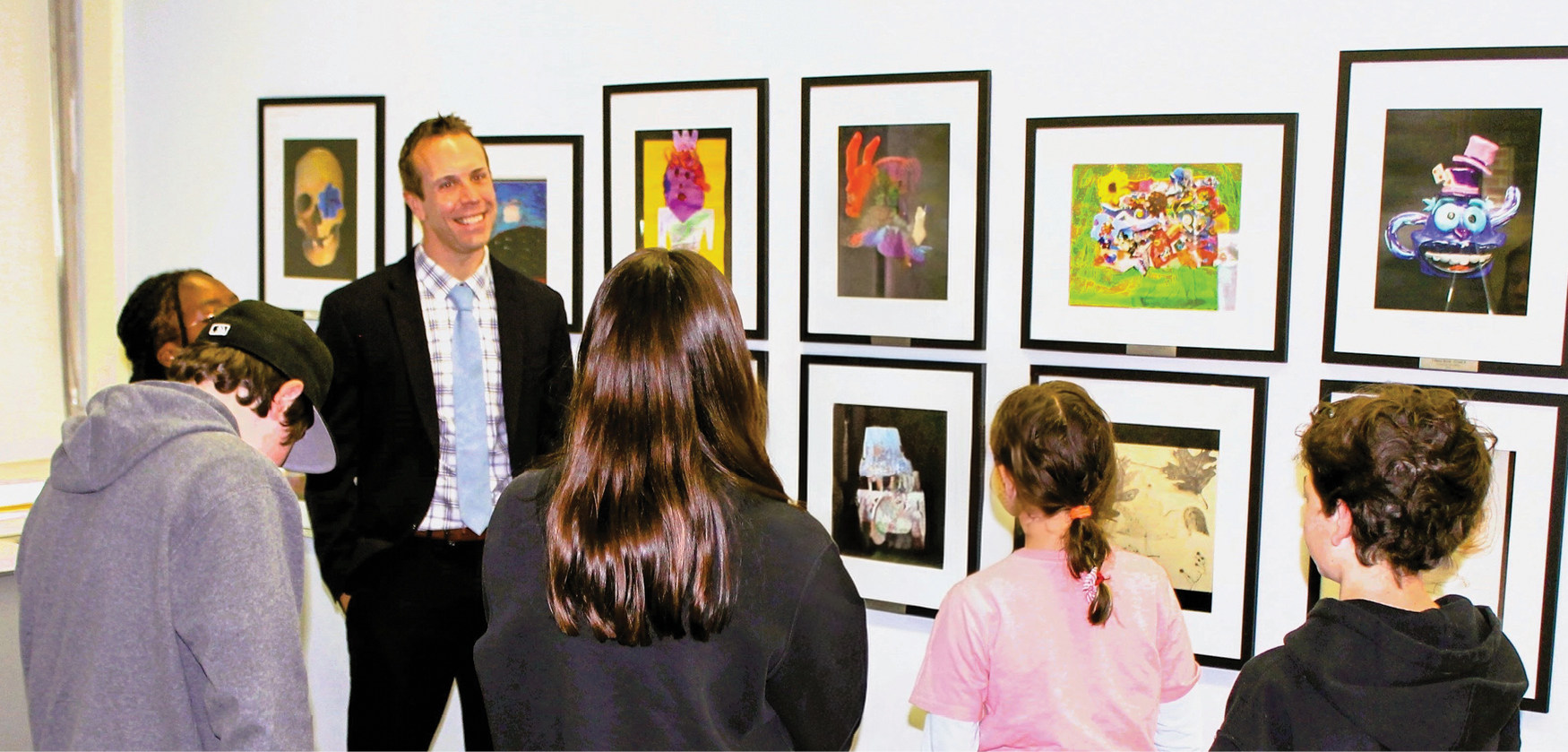 A man standing with a group of children in front of framed art on the wall