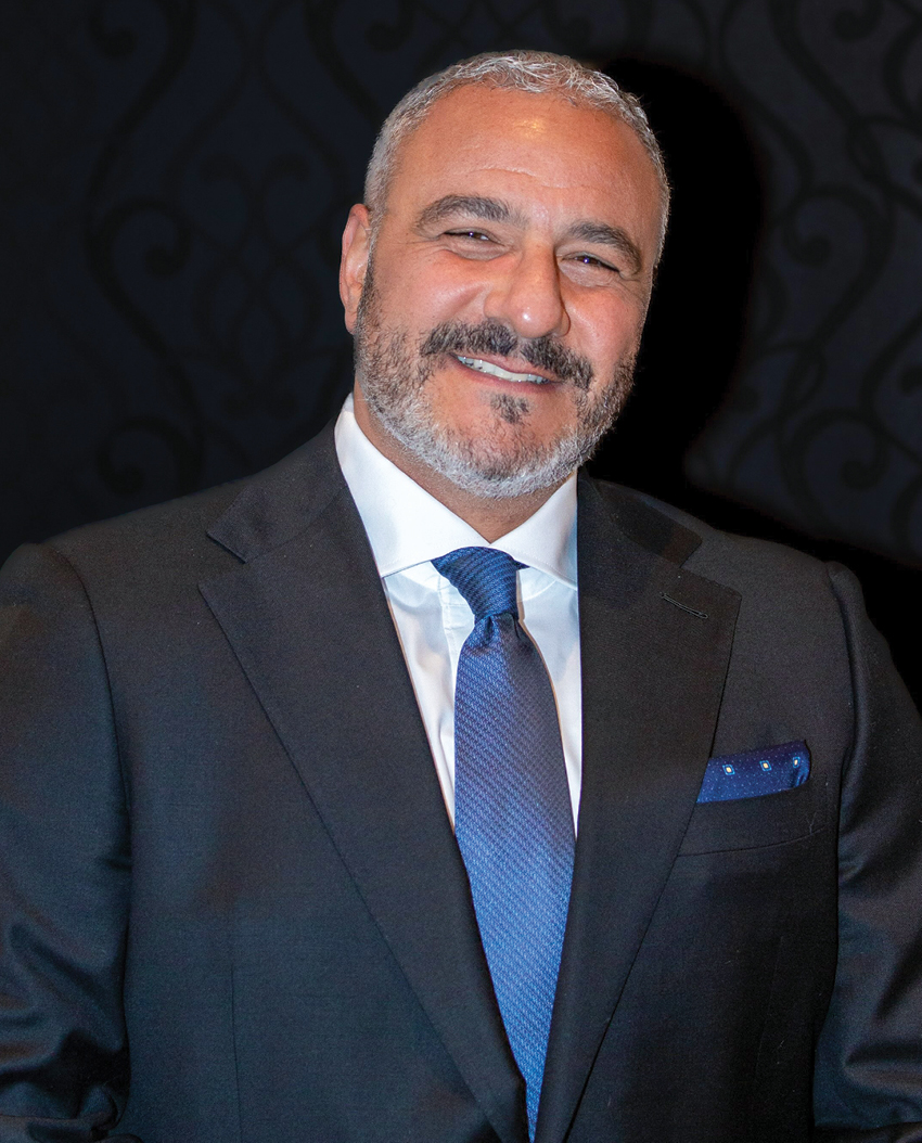 A headshot of a man in a black suit with blue tie