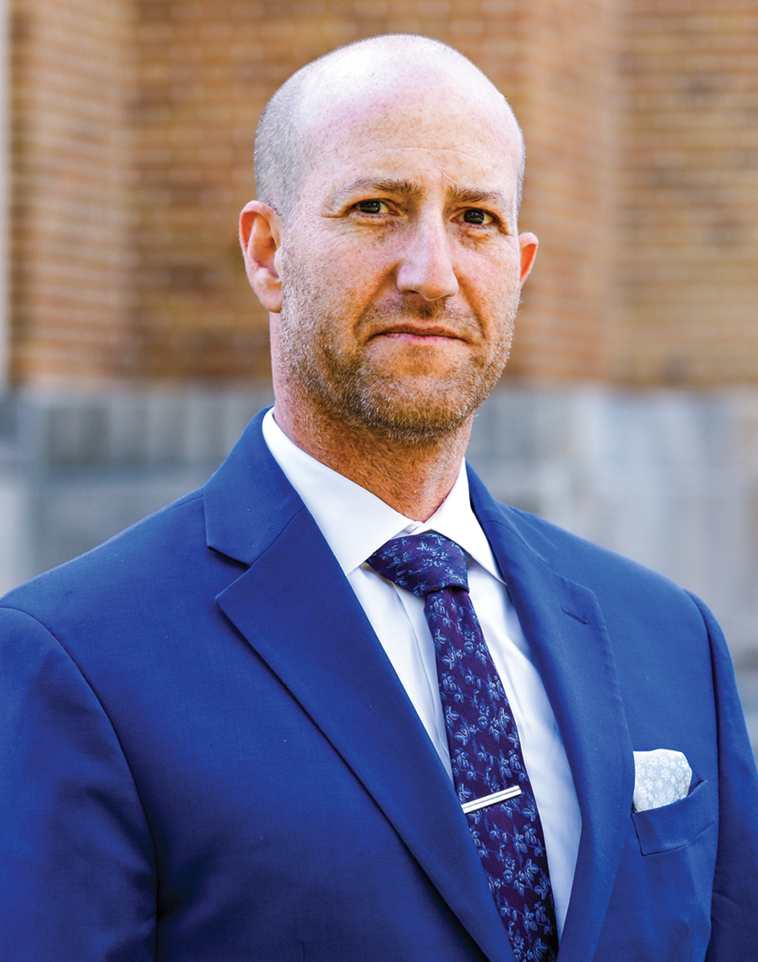 A headshot of a white man in a blue suit