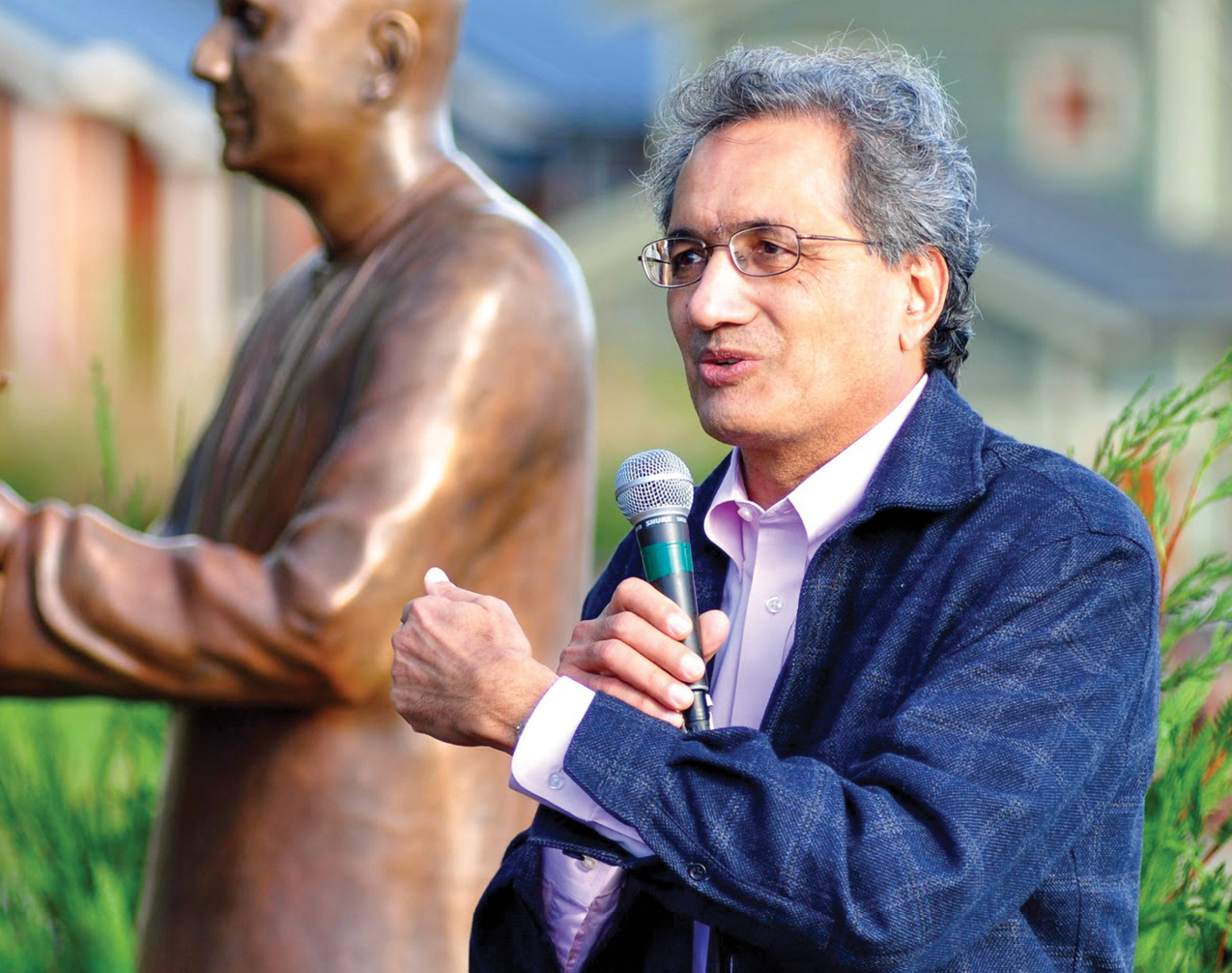 A man holding a microphone wearing a suit next to a statue
