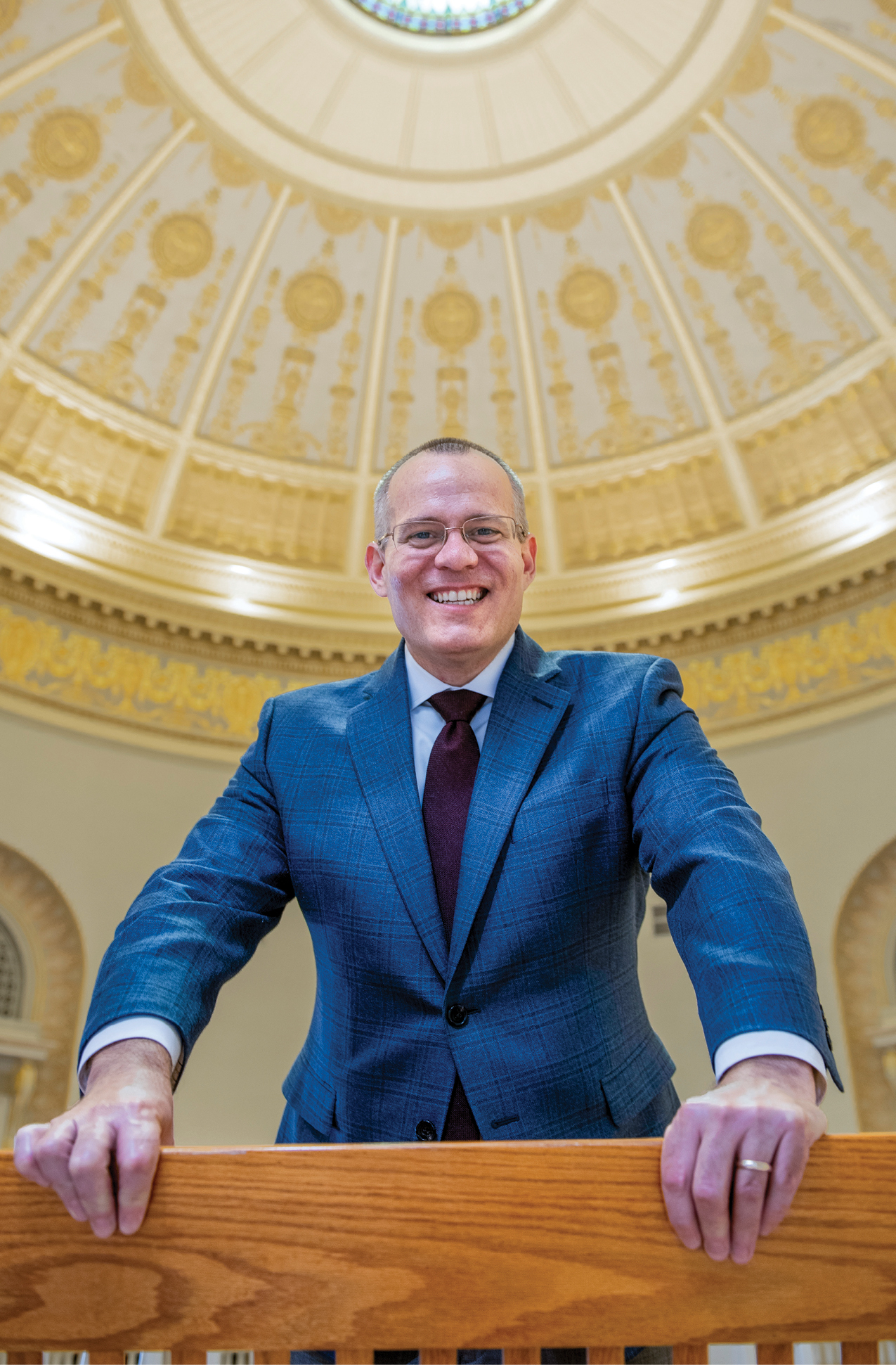 A man in a blue suit holding a wooden railing standing in a rotunda of an official building