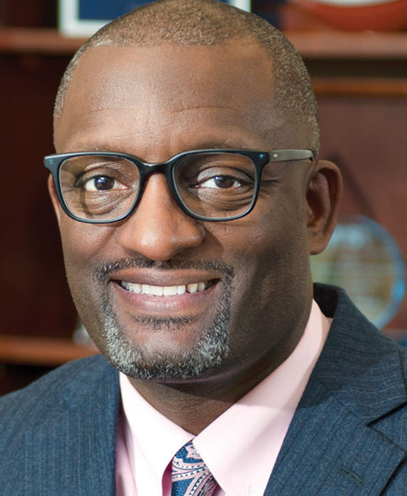 A headshot of a Black man with glasses wearing a suit