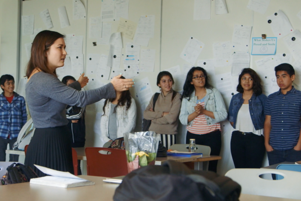 A teacher conducts a classroom exercise with students who stand along a wall